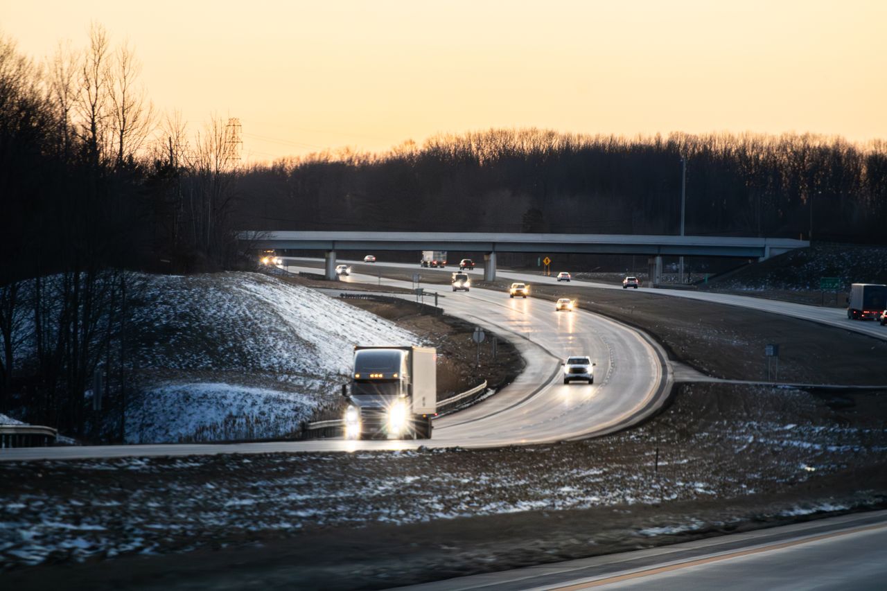 Cars and trucks on a highway at dusk with light snow
